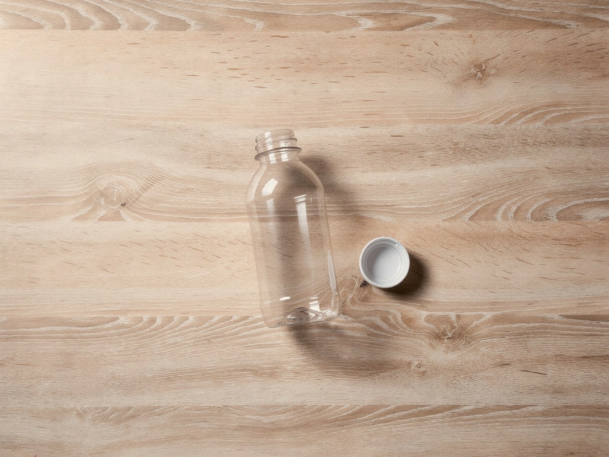 Die leere, klare Plastikflasche ohne Etikett steht allein auf dem Tisch, ihr weißer Schraubdeckel liegt daneben.