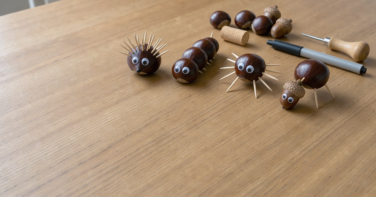 Vier fertige Kastanientiere stehen nebeneinander auf einem hellen Holztisch: ein Igel mit vielen Zahnstochern auf dem Rücken, eine Raupe aus mehreren Kastanien hintereinander, eine Spinne mit geraden Zahnstocherbeinen und eine Figur mit Eichelkopf, alle mit aufgeklebten Wackelaugen