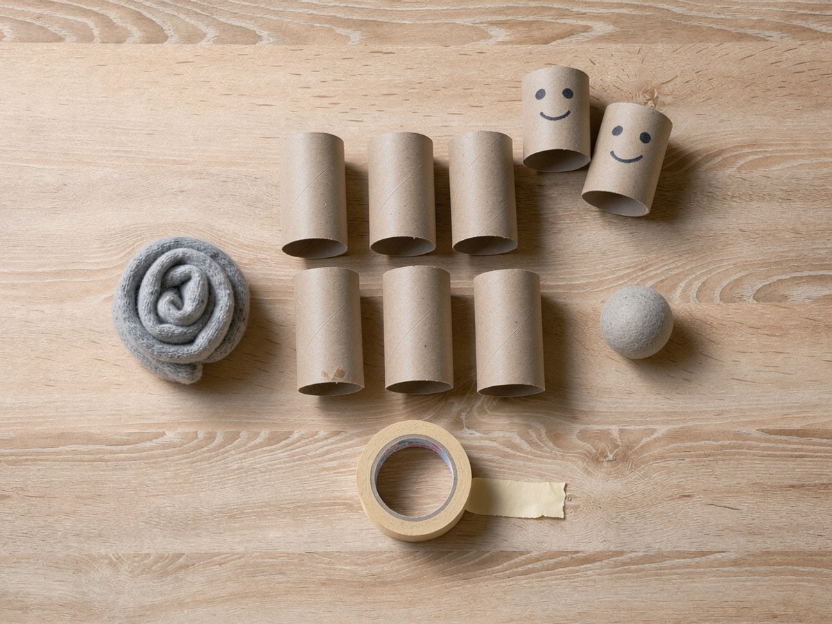 Material für das Kegelspiel von oben: sechs leere Klorollen, ein zusammengerollter Sockenball, ein kleiner Schaumstoffball und eine Rolle Kreppband
