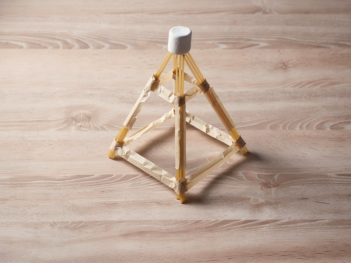 Der fertige Turm aus Dreiecken steht allein und unberührt auf dem freigeräumten Tisch, ganz oben sitzt der Marshmallow.