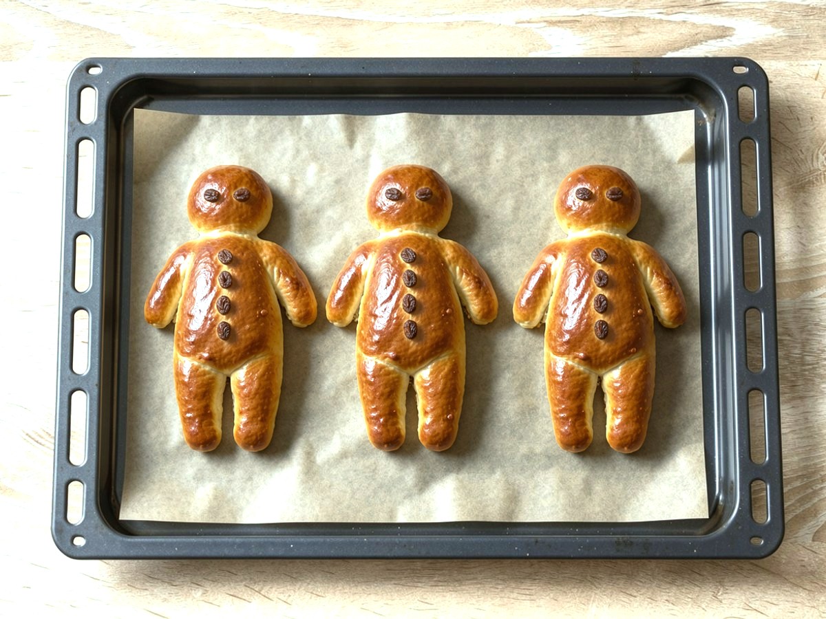 Von oben: dieselben drei Weckmänner, jetzt aufgegangen und goldbraun gebacken, mit glänzender Kruste und Rosinenaugen und -knöpfen, auf Backpapier im Backblech